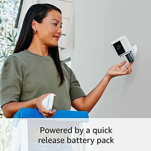 Woman installing a security camera with quick release battery pack.