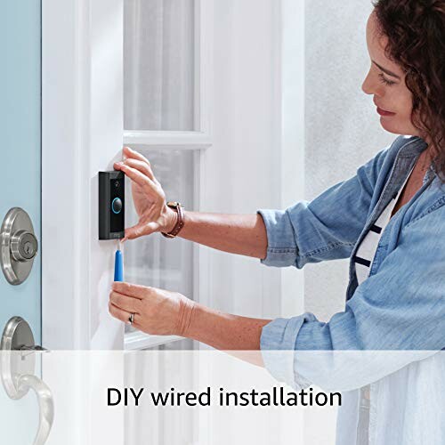 Woman installing a video doorbell next to a door.